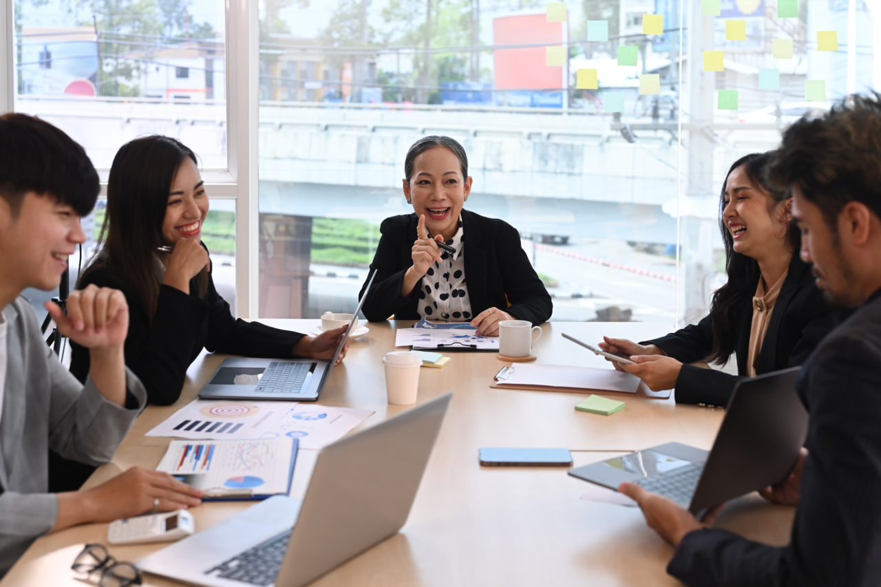 Attractive mature businesswoman speaking, training, explaining work process with diverse employees at corporate meeting.